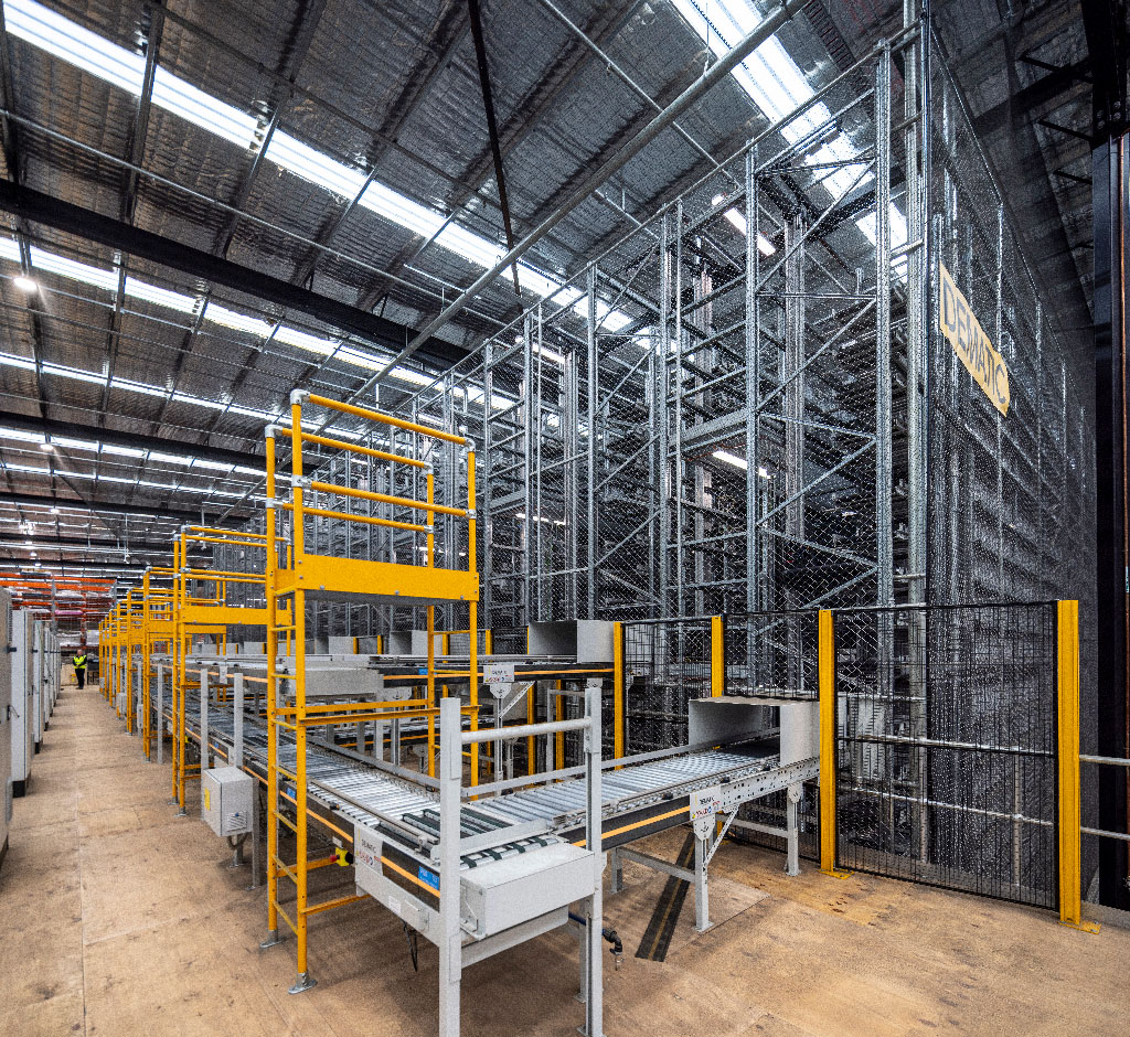 Industrial warehouse interior with high metal shelves and complex conveyor system. The space is vast and well-lit, emphasizing efficiency and order.