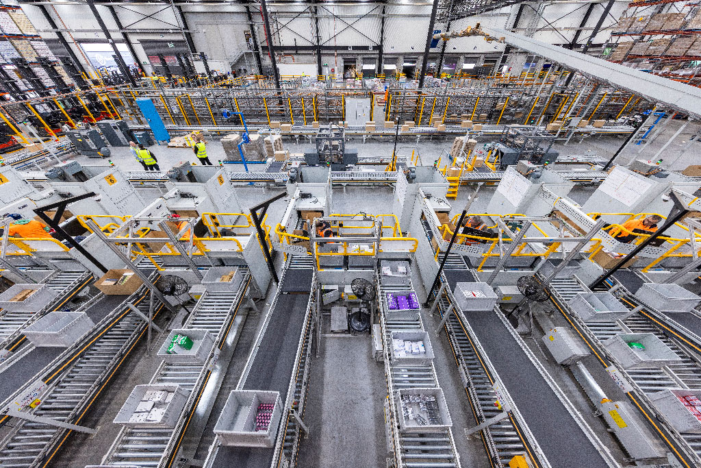 Aerial view of a bustling warehouse with multiple conveyor belts, packages, and workers in yellow vests, reflecting a high-tech, organized environment.