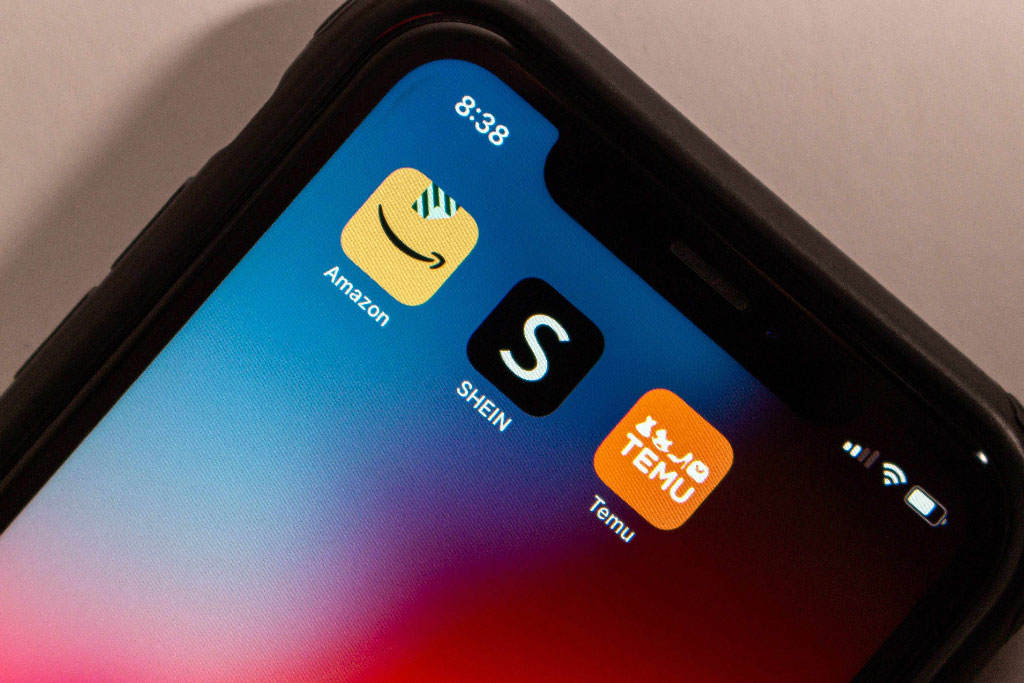 Close-up of a smartphone screen showing shopping apps: Amazon (yellow icon), SHEIN (black icon), and Temu (orange icon), set against a colorful background.
