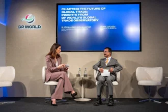 Two people sit on stage discussing global trade at a DP World event. A screen above displays the talk's title with a professional tone.