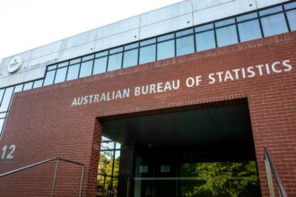Red brick building with "Australian Bureau of Statistics" in white letters. Modern glass accents, sunny day, and entrance with reflective windows.