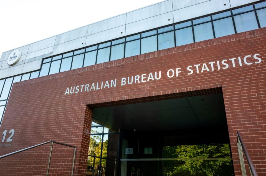 Red brick building with "Australian Bureau of Statistics" in white letters. Modern glass accents, sunny day, and entrance with reflective windows.