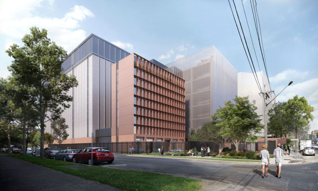 Street view of a modern, multi-story building with a sleek glass façade and brick accents. People walk along the sidewalk, and trees line the street.