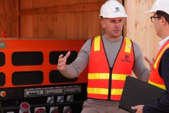 Two workers in safety gear discuss equipment at a construction site.