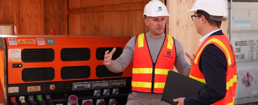 Two workers in safety gear discuss equipment at a construction site.