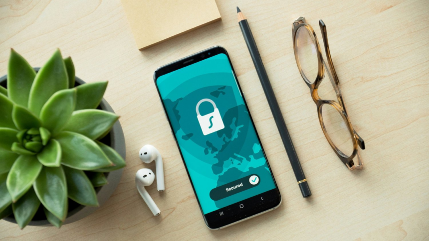 A mobile phone with a padlock on the lockscreen sitting on a table with a pencil and pair of glasses.