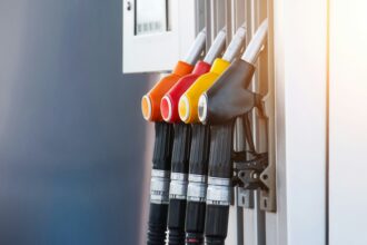 Close-up of four fuel pump nozzles in black, yellow, red and orange mounted on a petrol station pump, with the foreground in focus and a blurred background.