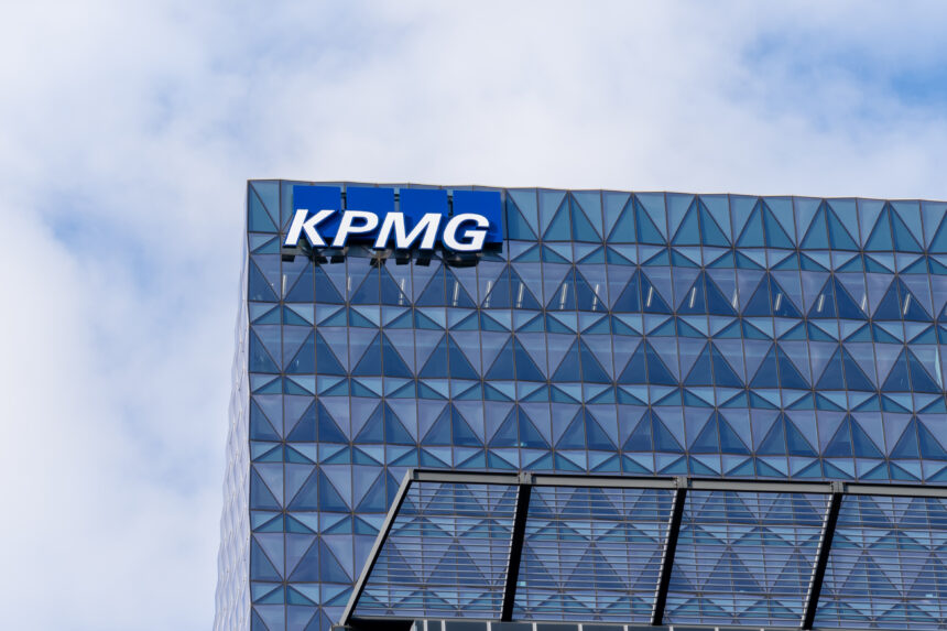 KPMG logo displayed on the upper facade of a modern glass office building against a cloudy blue sky.