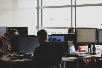 Three people sitting on office chairs looking at computer monitors.