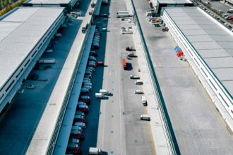 Aerial view of trucks outside giant logistics warehouse transit centre.