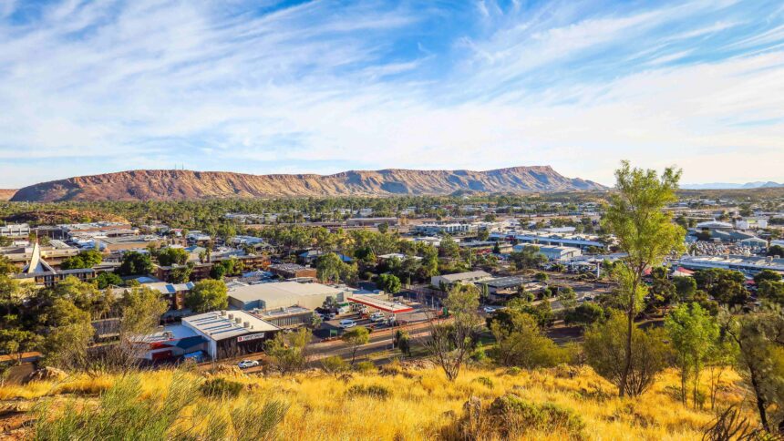 Elevated view over an Australian regional town, with buildings and trees beneath a prominent rocky mountain range.