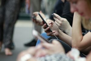Close-up of people sitting side by side using smartphones, with multiple hands holding mobile devices, illustrating social media and digital connectivity.