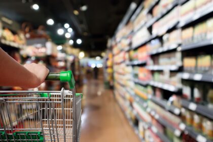 Woman hand hold shopping cart with Abstract blur supermarket aisle background.