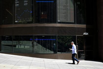 Exterior of the Australian Securities Exchange (ASX) building in Sydney, with stock market data displayed on digital screens and a pedestrian walking past the entrance.