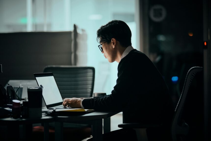 A man sits at his desk using a laptop.